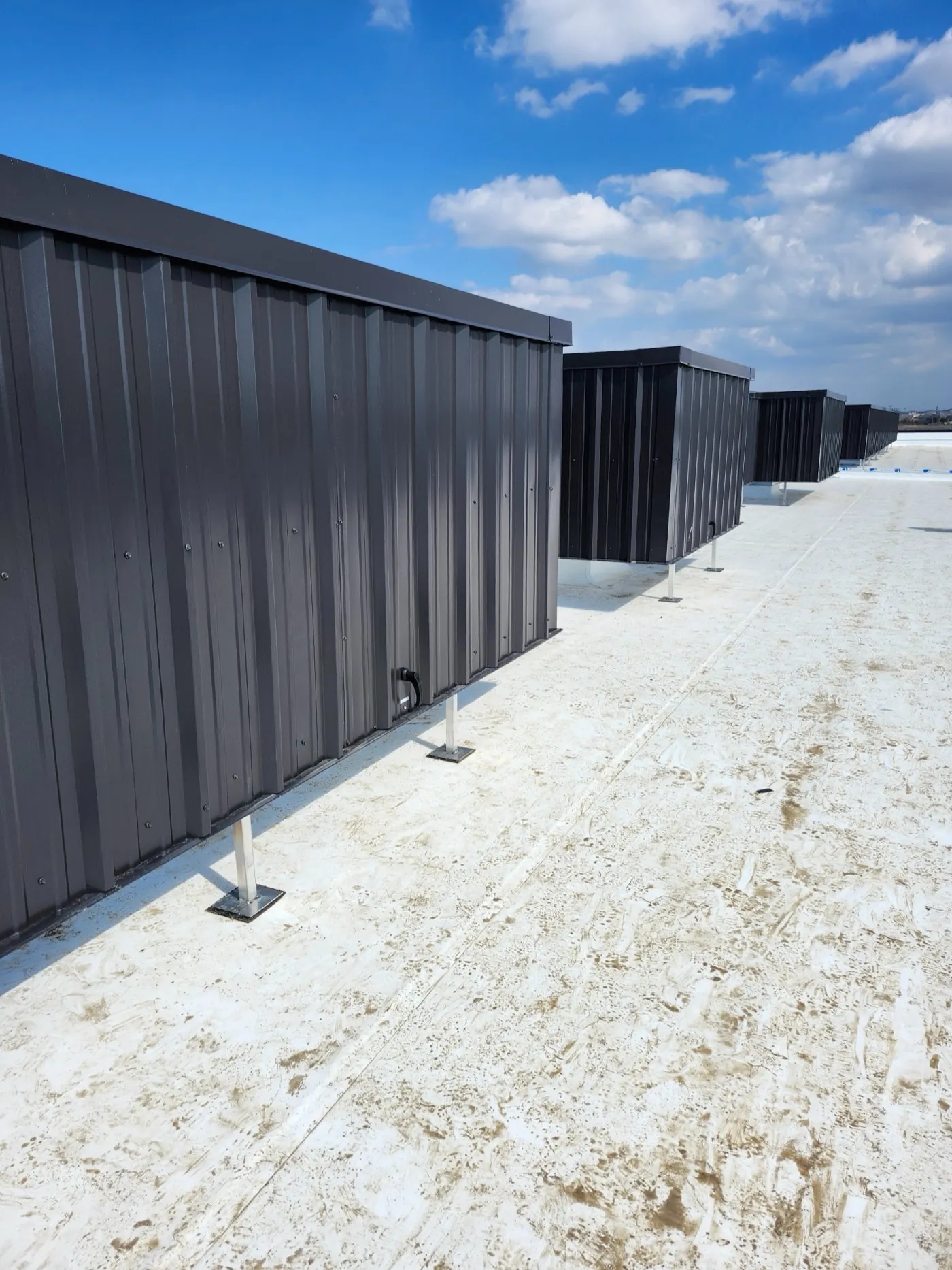 Row of dark gray solid-panel rooftop screens elevated on steel legs along a white commercial roof