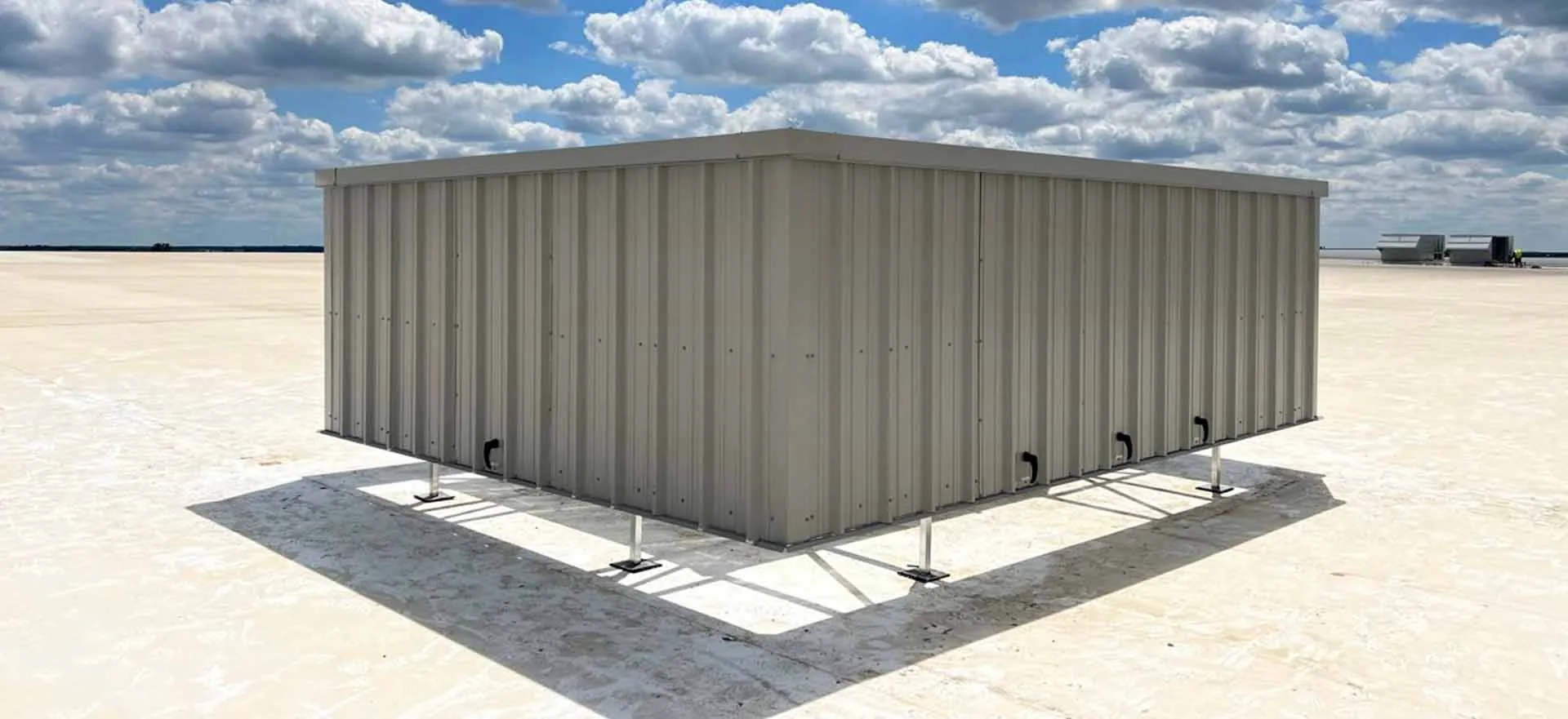 Beige solid-panel rooftop screen standing on steel legs above a white membrane roof